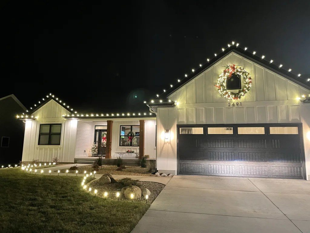 Warm white holiday roofline lighting with a lit wreath on a modern farmhouse