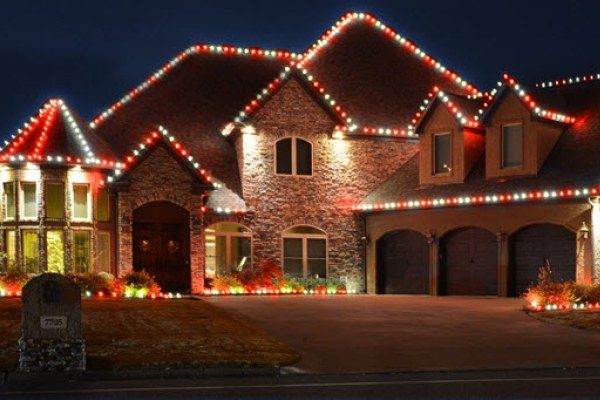 Red and white holiday roofline lighting on a stone and brick two-story home